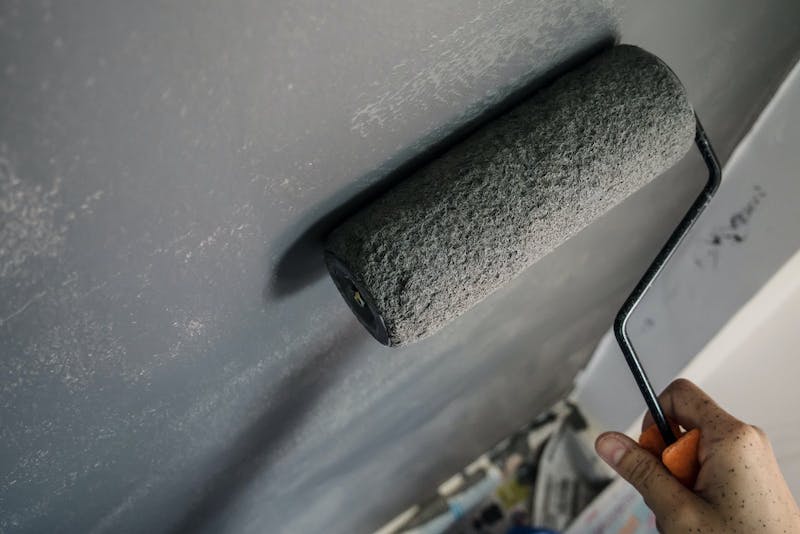 hand holding paint brush roller on wall with lick paint