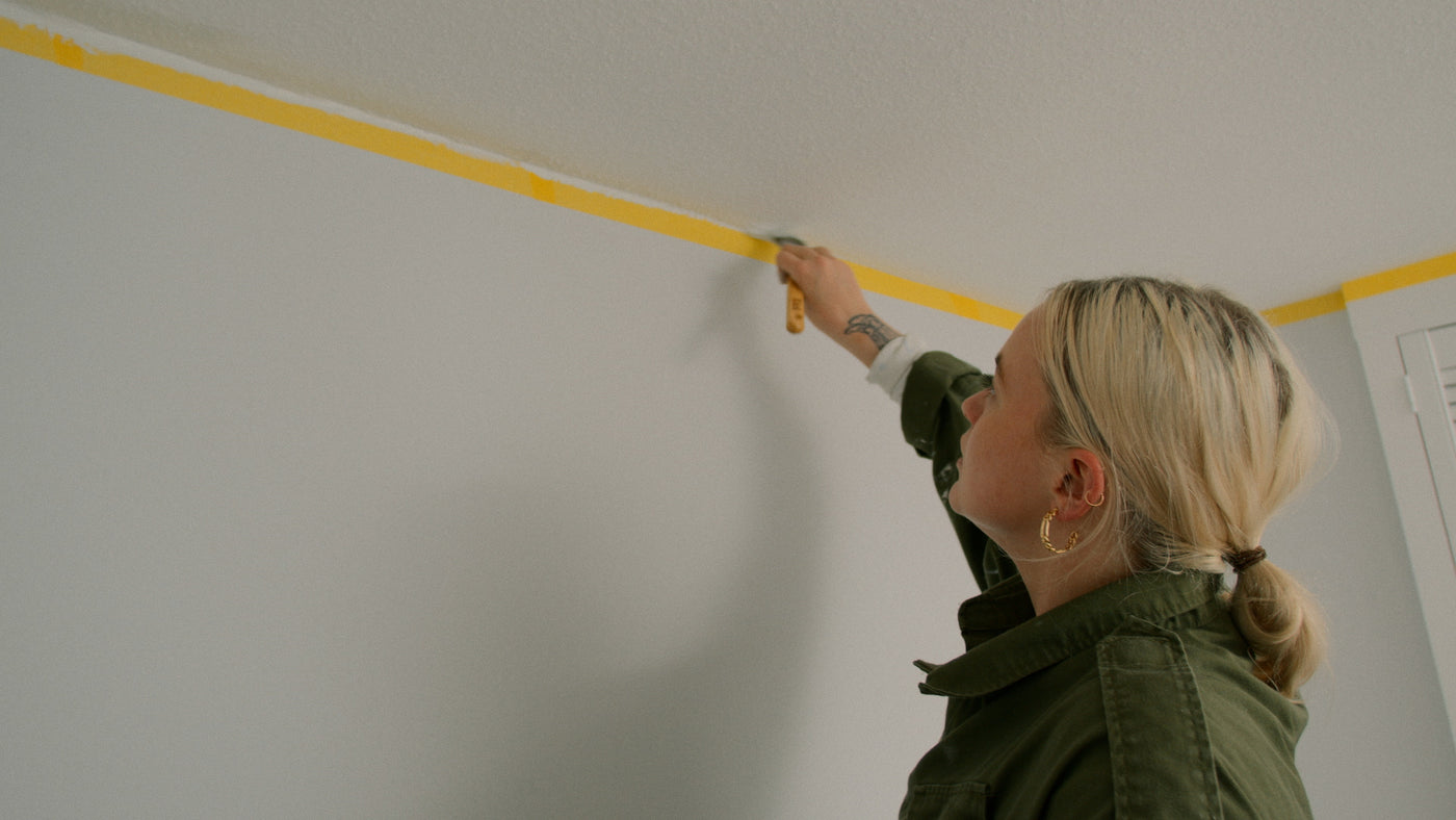 Woman painting a ceiling over masking tape 